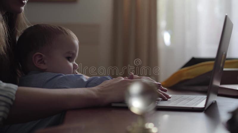 Las manos de la mujer que mecanograf? an en el ordenador port? til y el ni? o previenen a la madre de su trabajo Madre joven ocupada almacen de metraje de vídeo