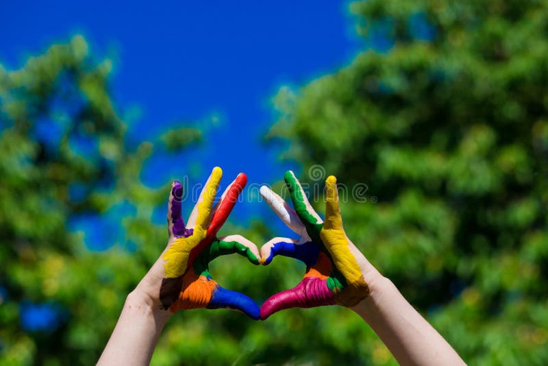 Las manos de los niños pintadas en colores brillantes hacen una forma del corazón en fondo de la naturaleza del verano fotografía de archivo Las manos de los niños pintadas en colores brillantes hacen una forma del corazón en fondo de la naturaleza del verano fotografía de archivo