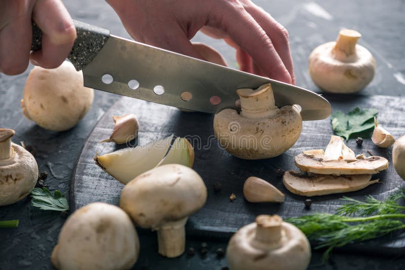 Las manos de las mujeres están cortando los champiñones con un cuchillo en la tabla de cocina oscura Cocinar platos de la seta Ci foto de archivo libre de regalías