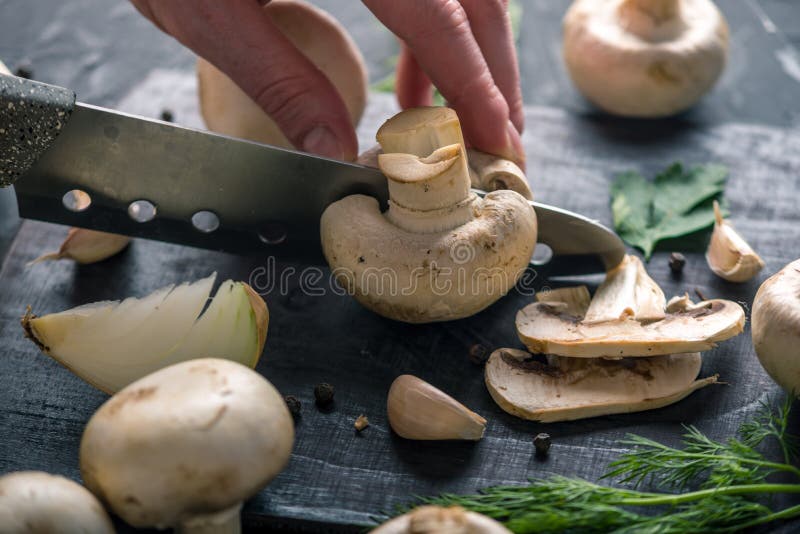 Las manos de las mujeres están cortando los champiñones con un cuchillo en la tabla de cocina oscura Cocinar platos de la seta Ci fotografía de archivo libre de regalías