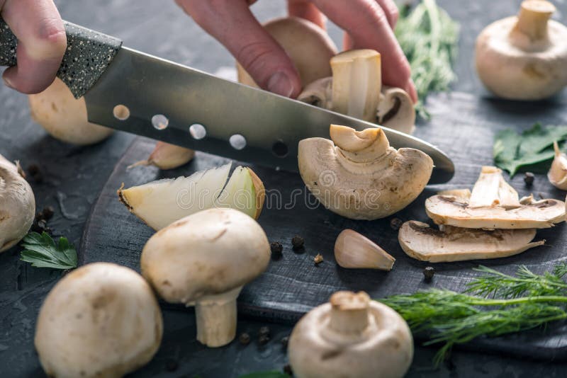 Las manos de las mujeres están cortando los champiñones con un cuchillo en la tabla de cocina oscura Cocinar platos de la seta Ci fotos de archivo