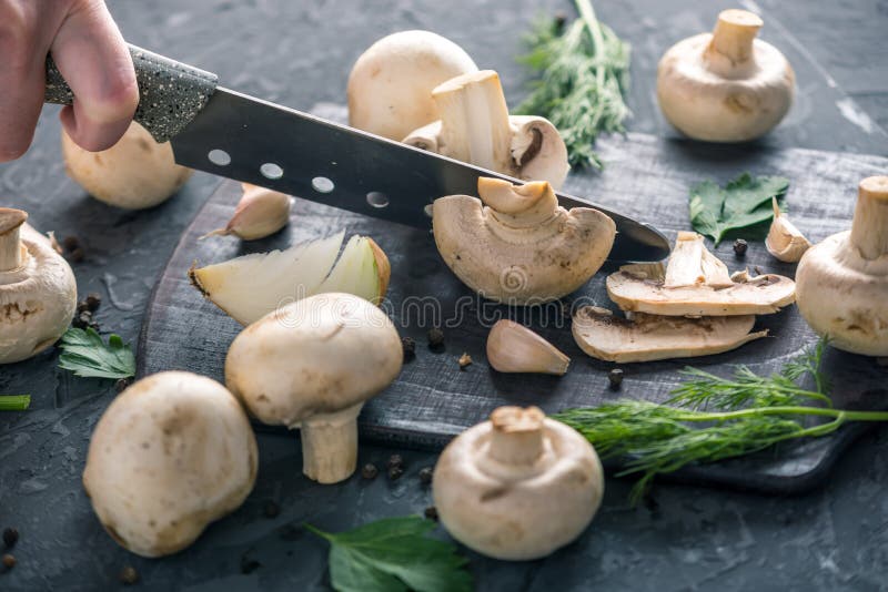 Las manos de las mujeres están cortando los champiñones con un cuchillo en la tabla de cocina oscura Cocinar platos de la seta Ci fotografía de archivo libre de regalías
