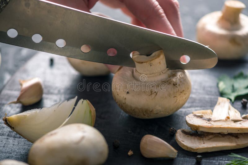 Las manos de las mujeres están cortando los champiñones con un cuchillo en la tabla de cocina oscura Cocinar platos de la seta Ci fotografía de archivo