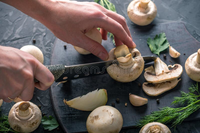 Las manos de las mujeres están cortando los champiñones con un cuchillo en la tabla de cocina oscura Cocinar platos de la seta Ci imagenes de archivo
