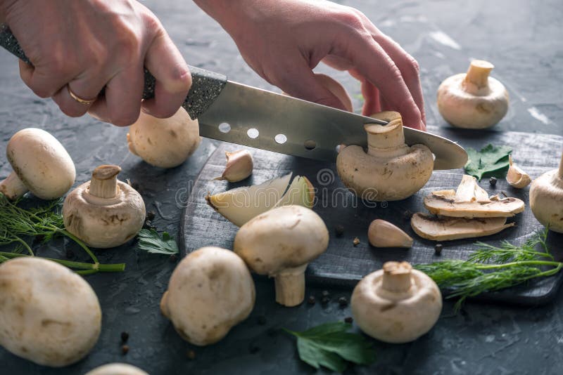 Las manos de las mujeres están cortando los champiñones con un cuchillo en la tabla de cocina oscura Cocinar platos de la seta Ci foto de archivo libre de regalías