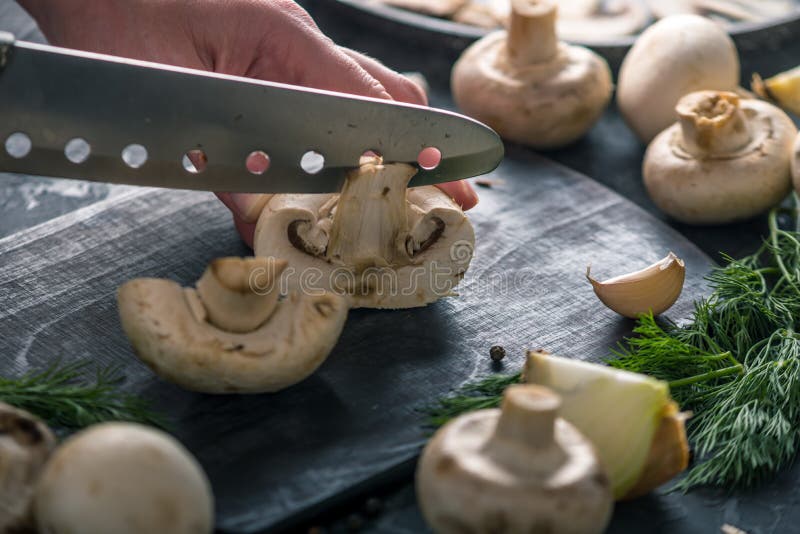 Las manos de las mujeres están cortando los champiñones con un cuchillo en la tabla oscura Cocinar platos de la seta imagen de archivo