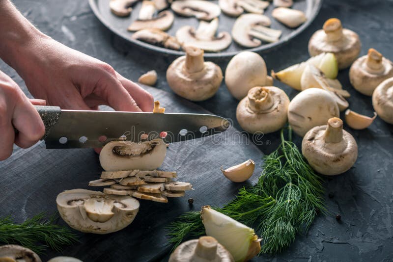 Las manos de las mujeres están cortando los champiñones con un cuchillo en la tabla oscura Cocinar platos de la seta foto de archivo