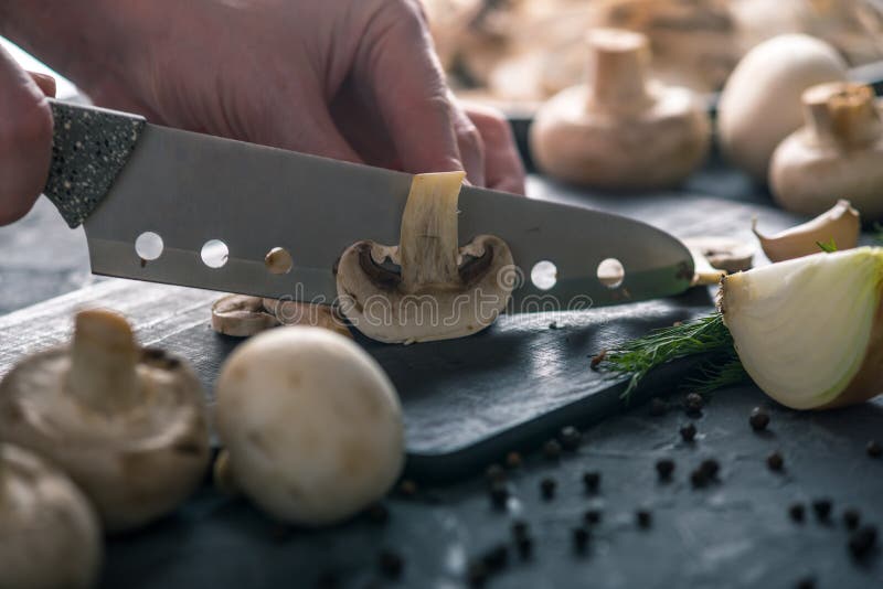 Las manos de las mujeres están cortando los champiñones con un cuchillo en la tabla oscura Concepto de cocinar platos de la seta imagen de archivo