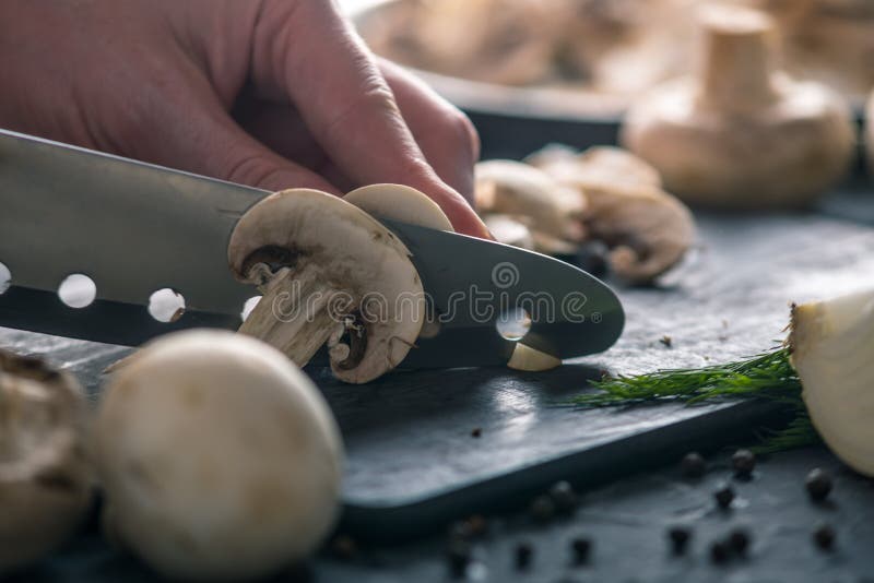 Las manos de las mujeres están cortando los champiñones con un cuchillo en la tabla oscura Concepto de cocinar platos de la seta imagen de archivo libre de regalías