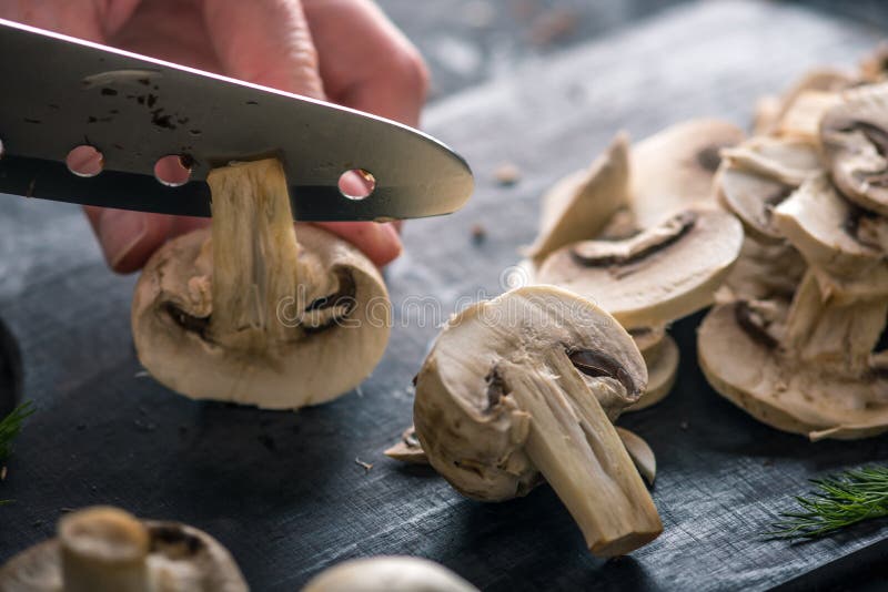 Las manos de las mujeres están cortando los champiñones con un cuchillo en la tabla oscura Concepto de cocinar platos de la seta fotos de archivo