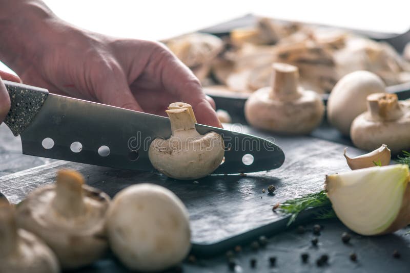 Las manos de las mujeres están cortando los champiñones con un cuchillo en la tabla oscura Concepto de cocinar platos de la seta foto de archivo