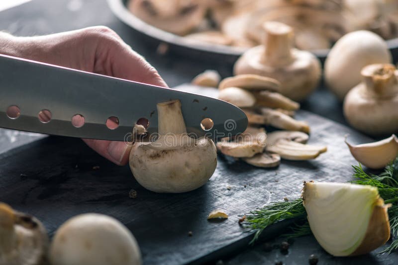 Las manos de las mujeres están cortando los champiñones con un cuchillo en la tabla oscura Concepto de cocinar platos de la seta foto de archivo libre de regalías