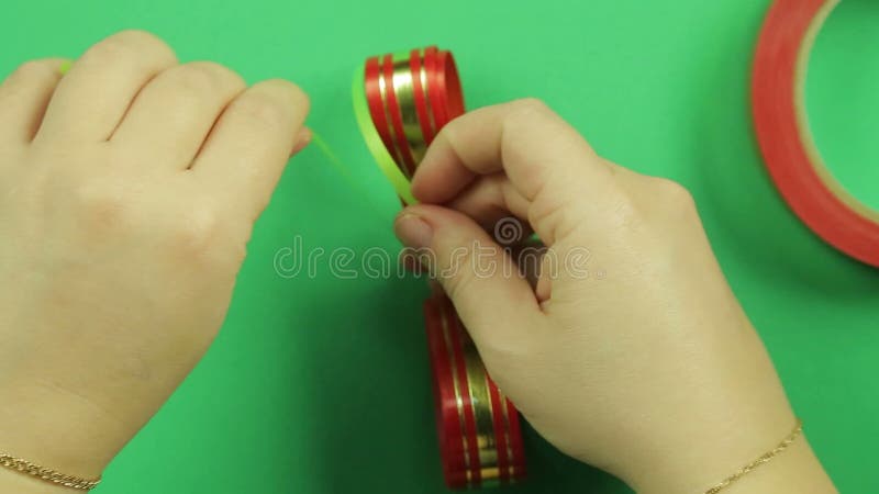 Las manos de las mujeres implican la forma de un espacio en blanco de la cinta roja con la cinta verde para hacer un arco del reg