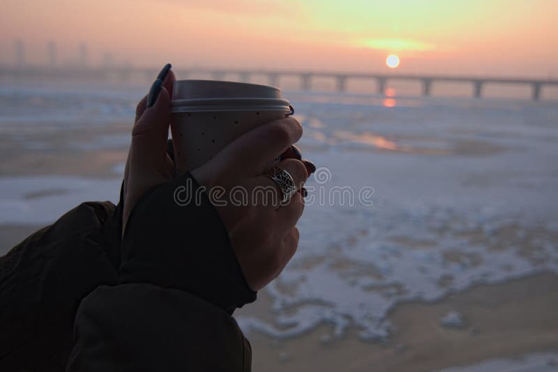 Las manos del ` s de las mujeres sostienen la taza de papel del café Salida del sol asombrosa en una mañana fresca del invierno e fotografía de archivo libre de regalías Las manos del ` s de las mujeres sostienen la taza de papel del café Salida del sol asombrosa en una mañana fresca del invierno e fotografía de archivo libre de regalías