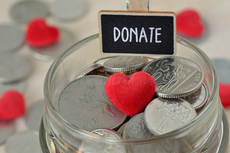Las monedas y el corazón en el tarro de cristal del dinero con donan la etiqueta - concepto de la caridad