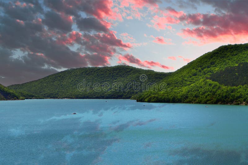Las montañas con el bosque verde en un lago apuntalan en el cielo hermoso de la puesta del sol con el fondo de las nubes fotos de archivo Las montañas con el bosque verde en un lago apuntalan en el cielo hermoso de la puesta del sol con el fondo de las nubes fotos de archivo