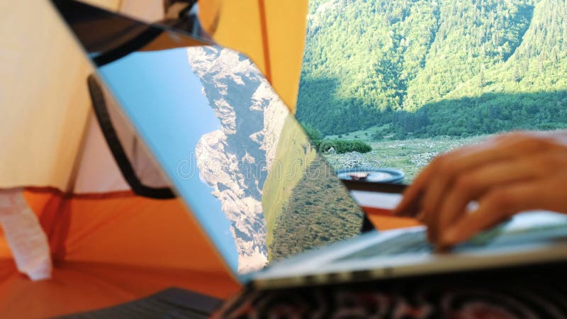 Las montañas se reflejan en la pantalla del ordenador portátil La mujer del Freelancer utiliza el ordenador en la tienda turístic