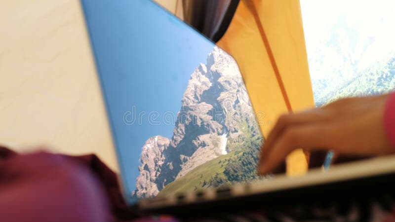 Las montañas se reflejan en la pantalla del ordenador portátil Una mujer utiliza un ordenador en una tienda turística, mecanograf