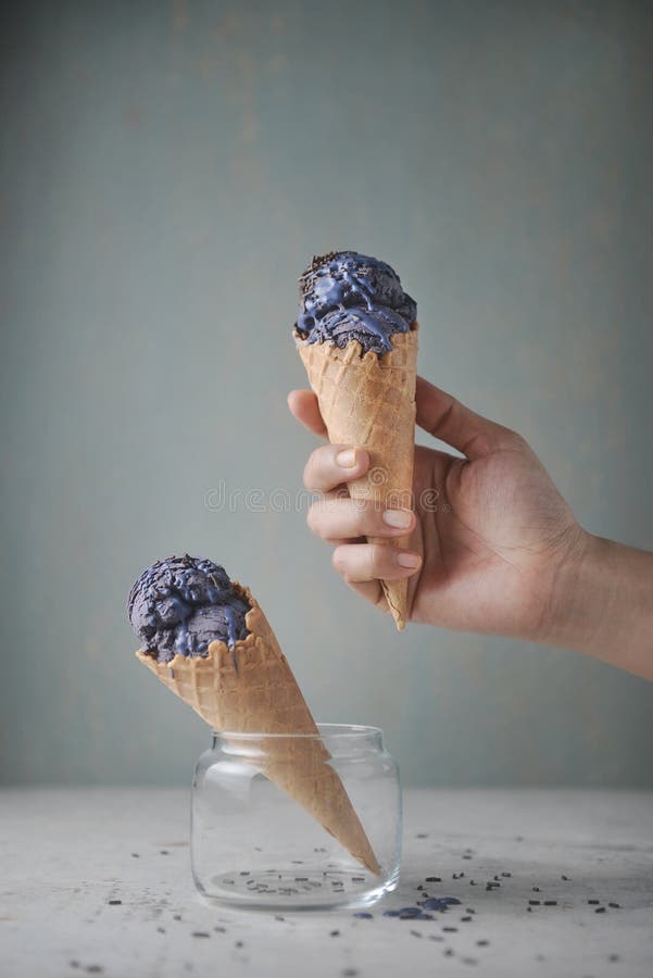 Las mujeres dan el cono de la galleta de la tenencia con helado del arándano y adornado con el chocolate asperja en fondo llano fotos de archivo libres de regalías Las mujeres dan el cono de la galleta de la tenencia con helado del arándano y adornado con el chocolate asperja en fondo llano fotos de archivo libres de regalías