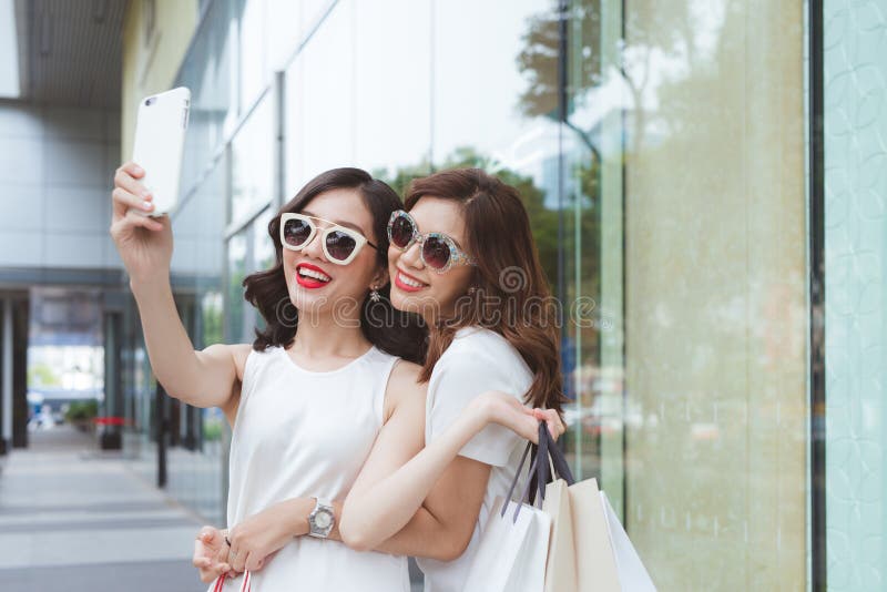 Las mujeres de los mejores amigos que toman el selfie en las caras divertidas que detienen a los compradores que llevan la moda d foto de archivo libre de regalías Las mujeres de los mejores amigos que toman el selfie en las caras divertidas que detienen a los compradores que llevan la moda d foto de archivo libre de regalías