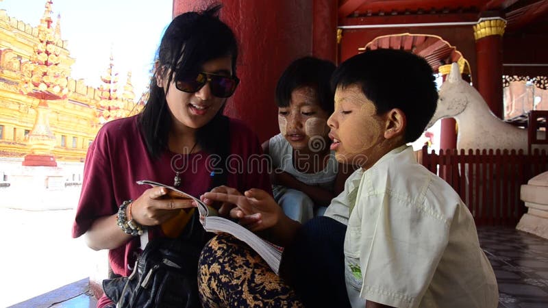 Las mujeres tailandesas enseñan los niños burmese al libro de lectura en la pagoda de Shwezigon