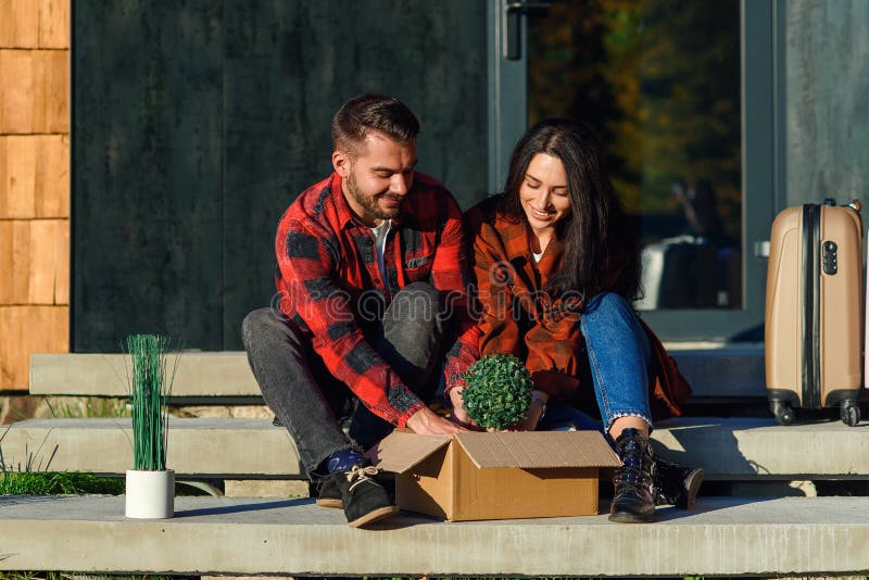Las parejas jóvenes que se sientan en las escaleras deportivos que desempaca las cajas después de pasar a la nueva casa. fotos de archivo