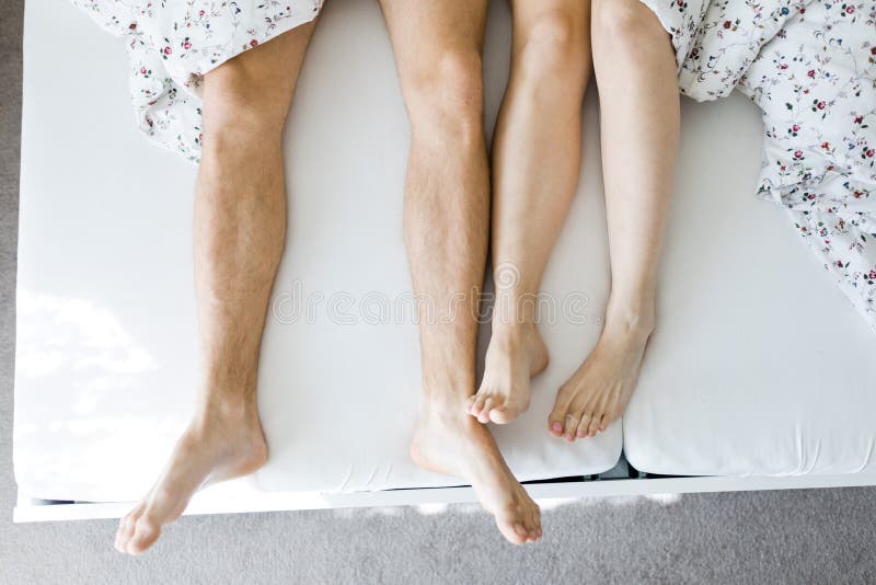 Las piernas del hombre y de la mujer en la hoja blanca de la cama cubierta parcialmente por la opinión superior del edredón foto de archivo Las piernas del hombre y de la mujer en la hoja blanca de la cama cubierta parcialmente por la opinión superior del edredón foto de archivo
