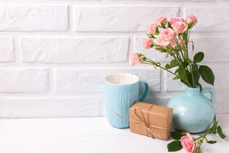 Las rosas rosadas florecen en el florero, caja con la actual y azul taza en wh fotografía de archivo Las rosas rosadas florecen en el florero, caja con la actual y azul taza en wh fotografía de archivo