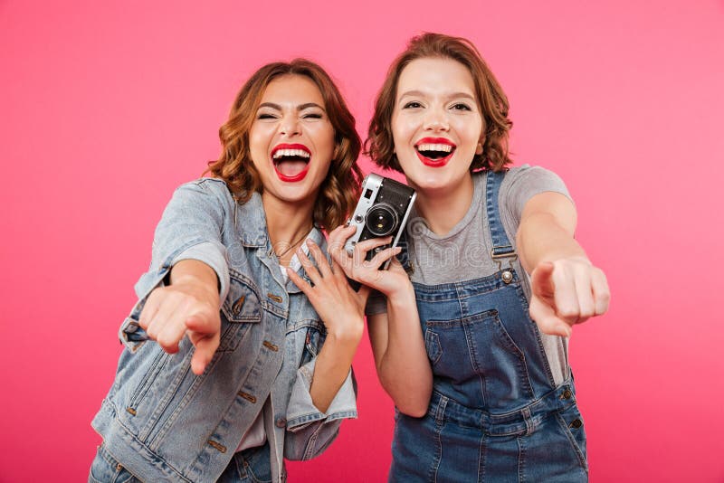 Las señoras felices hacen la foto por la cámara y señalar a usted foto de archivo Las señoras felices hacen la foto por la cámara y señalar a usted foto de archivo