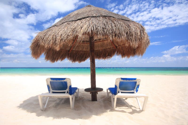 Beach chairs under the shade of a palapa thatched umbrella overlooking a beautiful tropical beach. Beach chairs under the shade of a palapa thatched umbrella overlooking a beautiful tropical beach