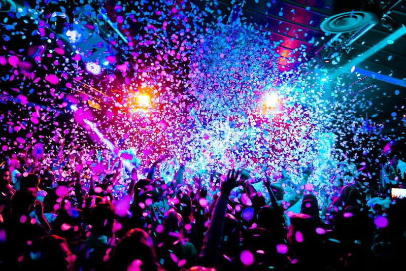 Las siluetas del concierto aprietan delante de luces brillantes de la etapa con confeti imagen de archivo Las siluetas del concierto aprietan delante de luces brillantes de la etapa con confeti imagen de archivo