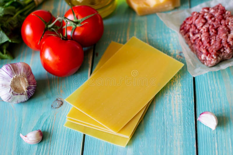Lasagna, tomatoes, minced meat and other ingredients. Blue wooden background. Italian cuisine royalty free stock photography Lasagna, tomatoes, minced meat and other ingredients. Blue wooden background. Italian cuisine royalty free stock photography