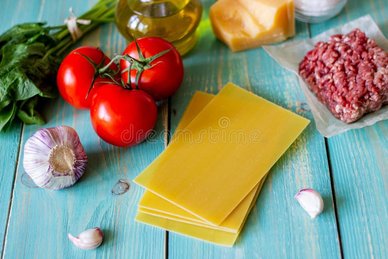 Lasagna, tomatoes, minced meat and other ingredients. Blue wooden background. Italian cuisine stock images Lasagna, tomatoes, minced meat and other ingredients. Blue wooden background. Italian cuisine stock images