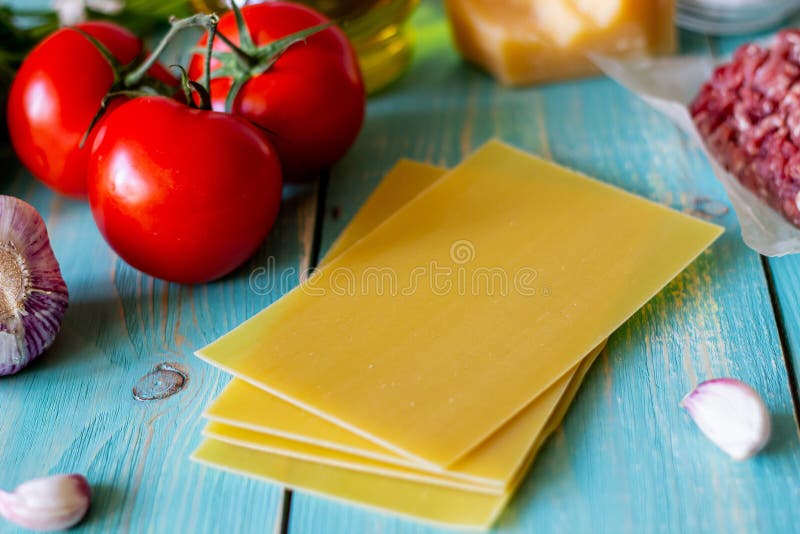 Lasagna, tomatoes, minced meat and other ingredients. Blue wooden background. Italian cuisine royalty free stock image Lasagna, tomatoes, minced meat and other ingredients. Blue wooden background. Italian cuisine royalty free stock image