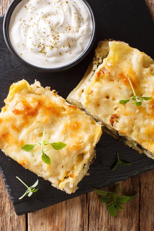 White lasagna with chicken, forest mushrooms, cheese and bechamel sauce close-up on a slate plate. Vertical top view from above. White lasagna with chicken, forest mushrooms, cheese and bechamel sauce close-up on a slate plate. Vertical top view from above