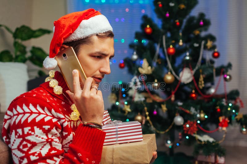 Lasciato solo per Natale Un uomo triste che parla con degli amici con uno smartphone che tiene scatole regalo Festeggiamenti per immagini stock Lasciato solo per Natale Un uomo triste che parla con degli amici con uno smartphone che tiene scatole regalo Festeggiamenti per immagini stock