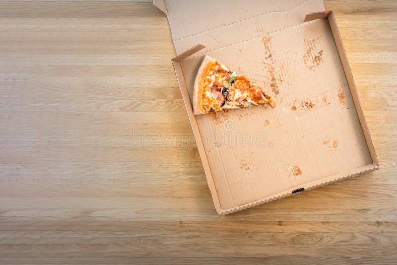 The last slice of pizza in the cardboard box on the wooden table in restaurant. Top view and copy space for text