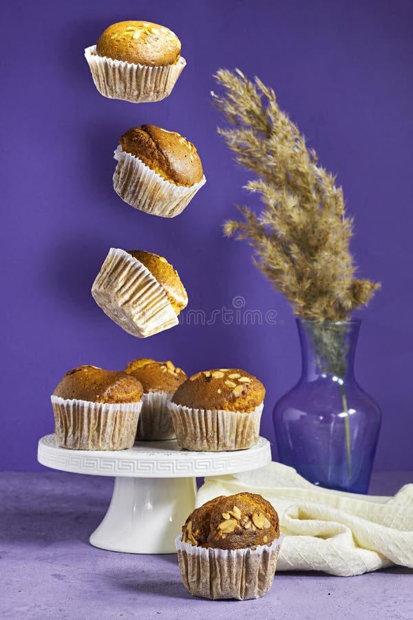 Latające muffinki z orzechów waniliowych w papierowych kubkach z wazonem z trzciny na fioletowym tle fotografia stock