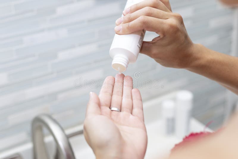 Latina Woman Putting Skin Care Cream on Her Hand. she Has a Towel on