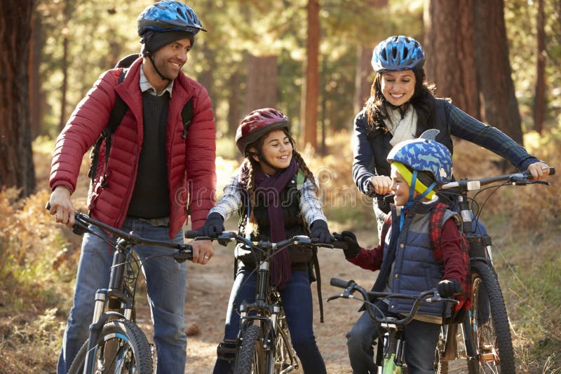 Latinamerikansk familj på cyklar i en skog som ser de royaltyfri bild Latinamerikansk familj på cyklar i en skog som ser de royaltyfri bild