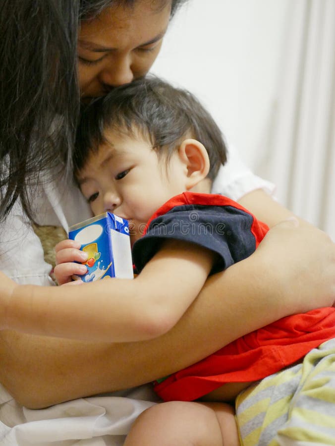 Latte alimentare della neonata asiatica sonnolenta da un cartone con paglia immagini stock libere da diritti Latte alimentare della neonata asiatica sonnolenta da un cartone con paglia immagini stock libere da diritti