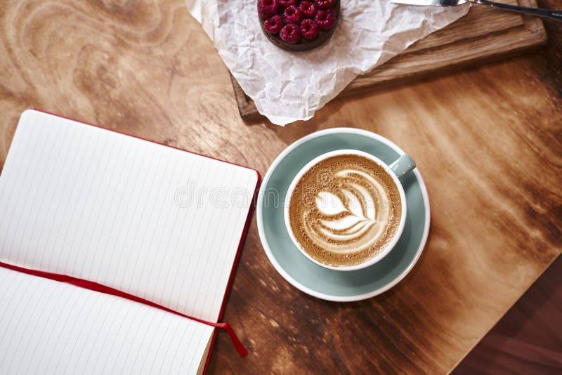 Latte della tazza di caffè sulla tavola di legno o fondo da sopra Pranzando in caffè Taccuino aperto, spazio per il modello di pr fotografia stock libera da diritti