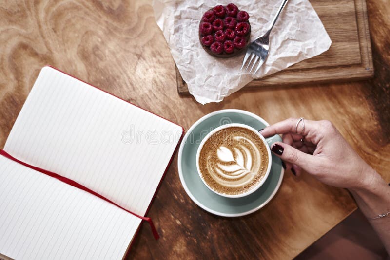 Latte della tazza di caffè sulla tavola di legno o fondo in mani della donna da sopra Pranzando in caffè Taccuino aperto fotografia stock