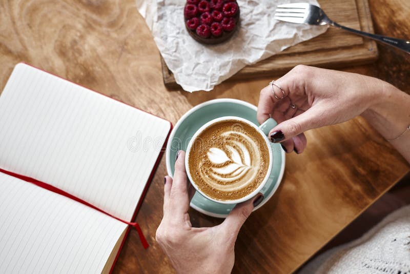 Latte della tazza di caffè sulla tavola di legno o fondo in mani della donna da sopra Pranzando in caffè Taccuino aperto fotografia stock libera da diritti