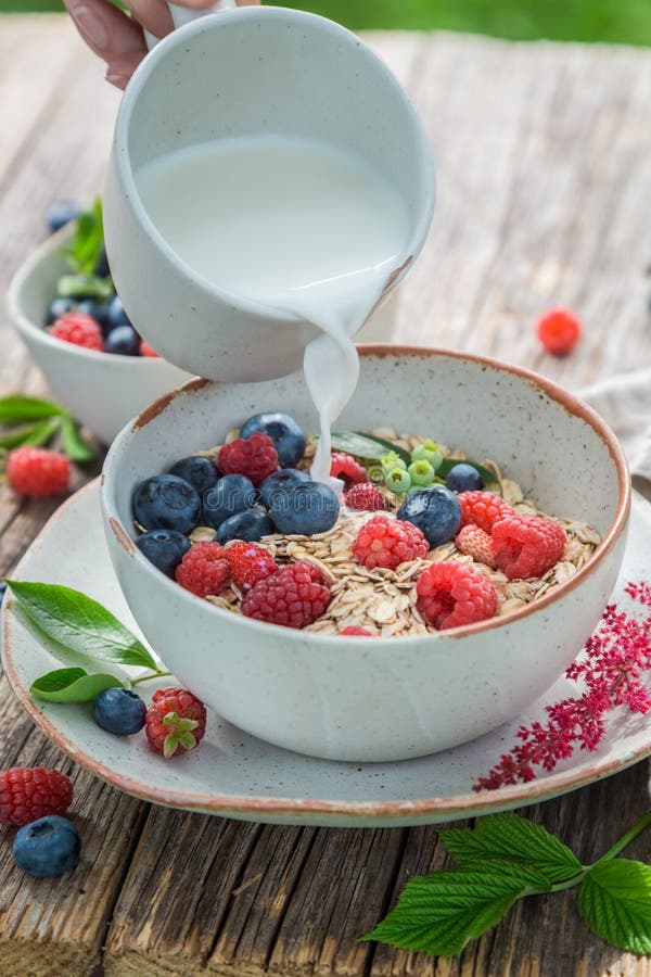 Latte di versamento in granola con i mirtilli ed i lamponi freschi fotografie stock Latte di versamento in granola con i mirtilli ed i lamponi freschi fotografie stock