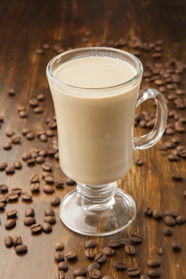 Latte i en glasmug färdig att dricka. Utsökt koffellatte på en träbakgrund omgiven av rostade kaffebönor