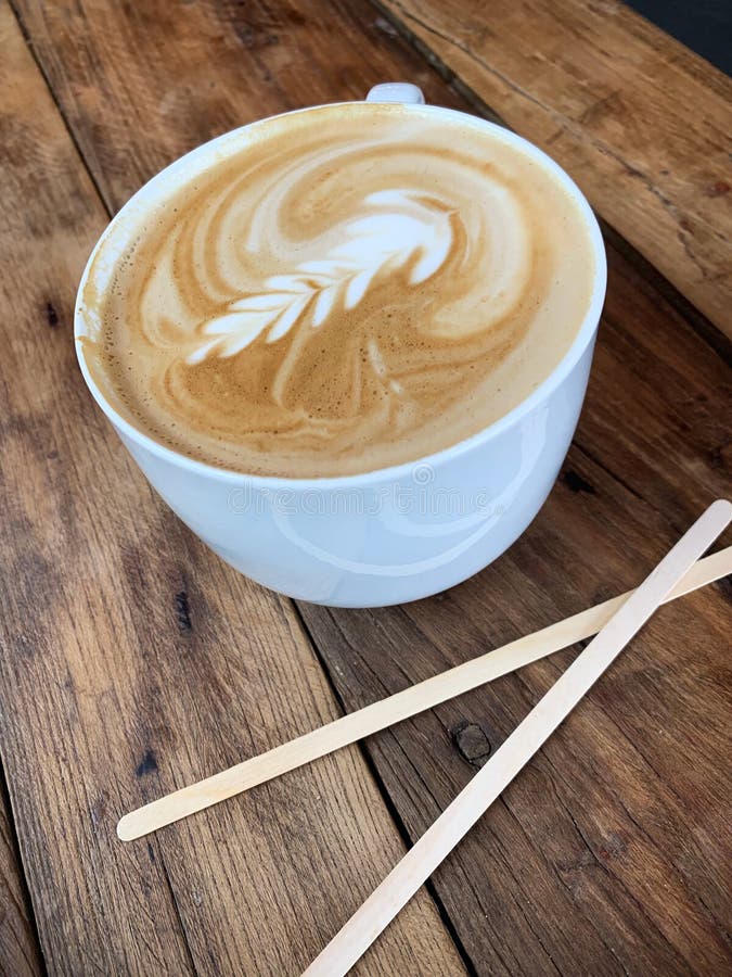 Latte med design i skumet i ett vitt rånar på träbakgrund arkivbild