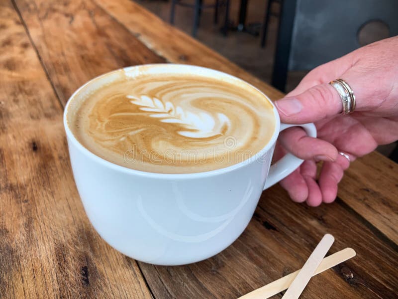 Latte med design i skumet i ett vitt rånar på träbakgrund royaltyfri fotografi