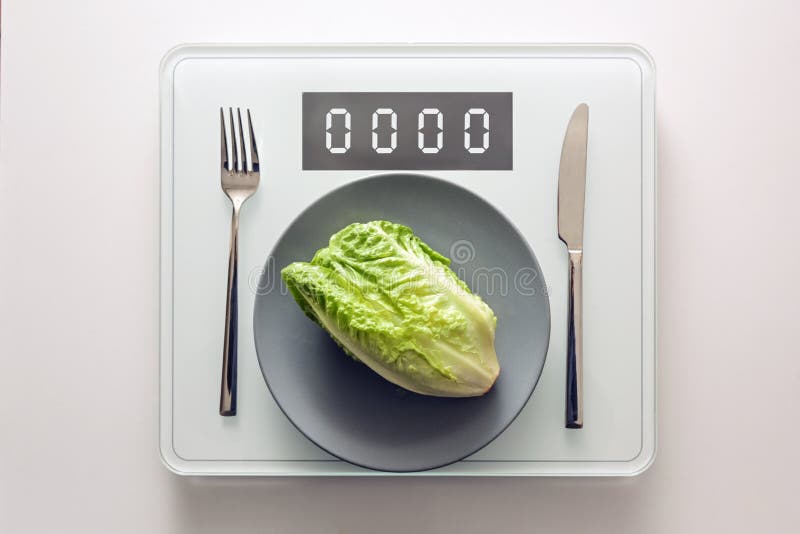 Fresh green lettuce or baby cos on a gray plate and cutlery on a digital weight scale showing zero, healthy diet and lose weight concept, copy space, high angle view from above. Fresh green lettuce or baby cos on a gray plate and cutlery on a digital weight scale showing zero, healthy diet and lose weight concept, copy space, high angle view from above