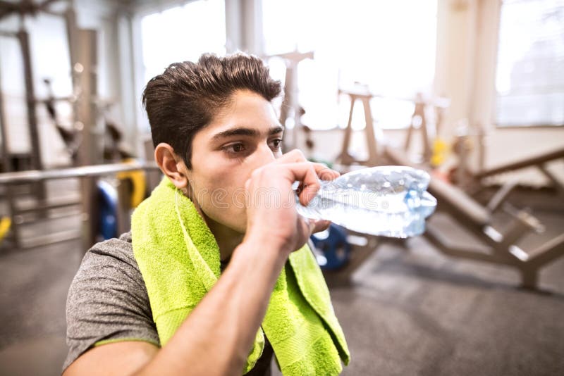 Latynoski mężczyzna odpoczywa w gym, woda pitna, ręcznik wokoło szyi fotografia royalty free Latynoski mężczyzna odpoczywa w gym, woda pitna, ręcznik wokoło szyi fotografia royalty free